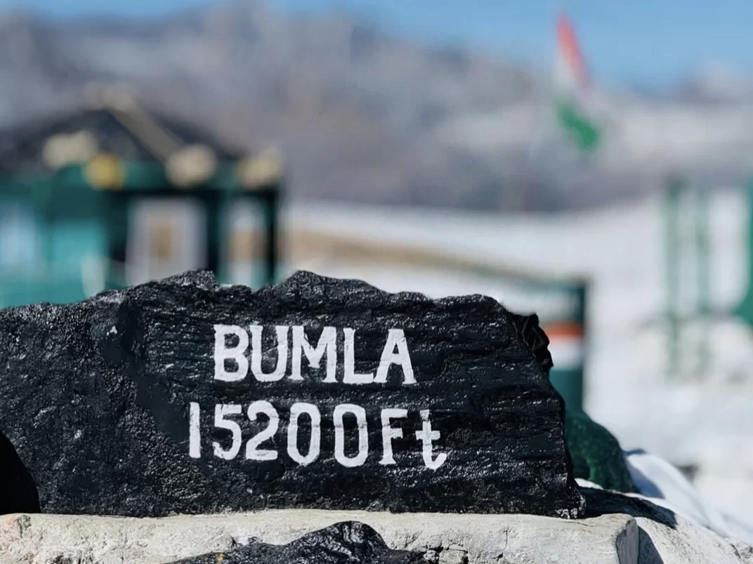 Bum La Pass 15200 ft Tawang Arunachal Pradesh iconic black stone signboard Indian Chinese flags snowy mountains army post blue sky high altitude Indo-China border, perfect Arunachal tour packages.