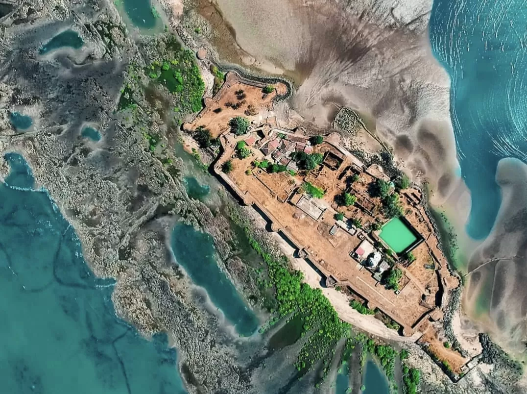 Aerial view of Kolaba Fort near Alibaug, showing its rectangular coastal ramparts surrounded by tidal waters, inner courtyards with temples and greenery, and a distinct green rectangular water tank inside the fort.