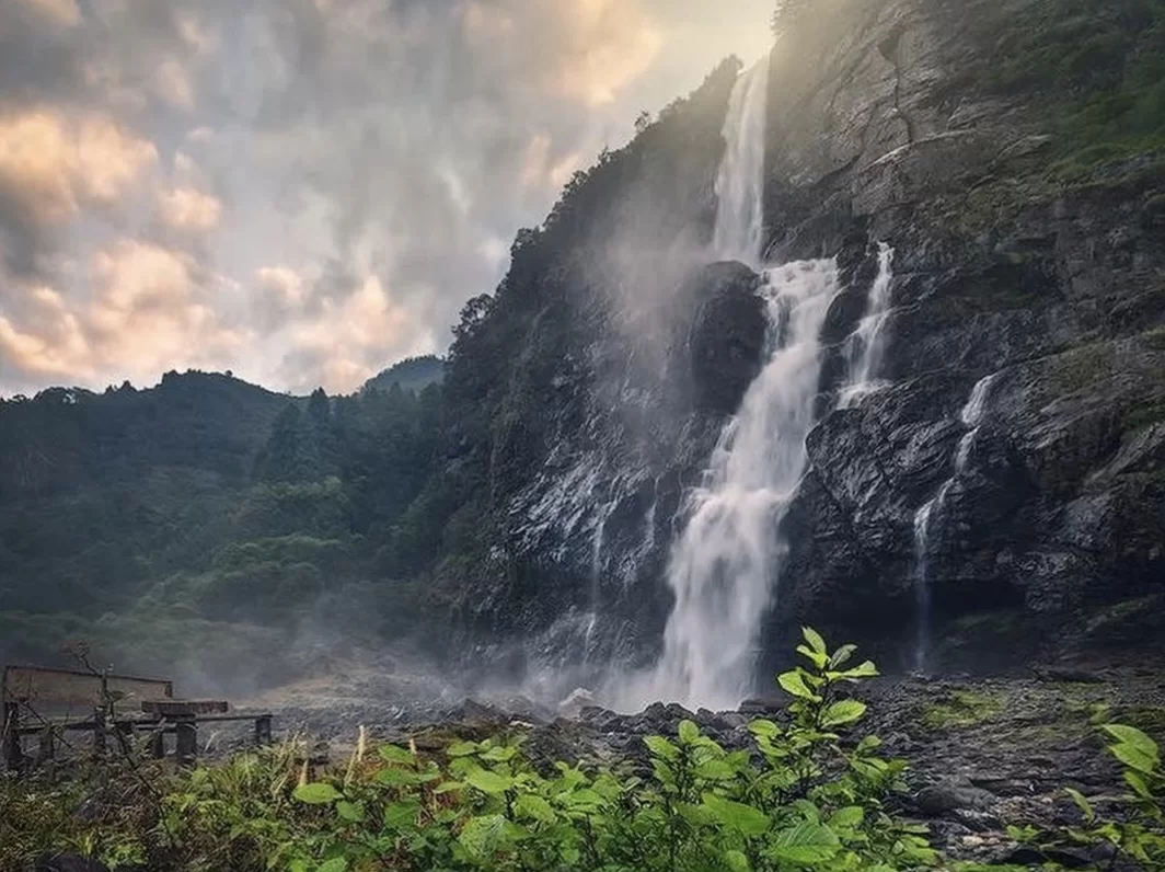 Nuranang Waterfall (Jang Falls) Tawang Arunachal Pradesh majestic 100m cascade misty rocky cliffs lush green forest golden sunset glow wooden bench foreground, perfect scenic Northeast India tour packages.