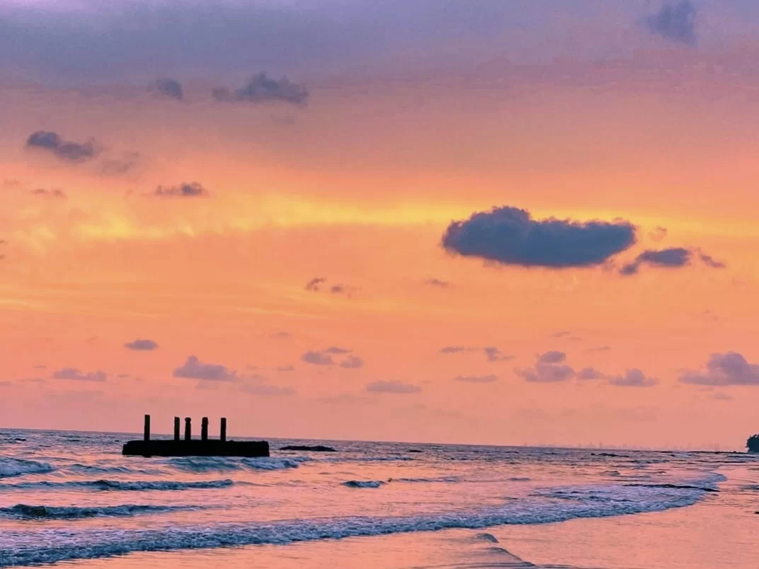 Sunset silhouettes of shipwreck pillars at Kihim Beach Alibaug, featuring orange-purple skies, Arabian Sea waves, perfect romantic experience Konkan tour package.