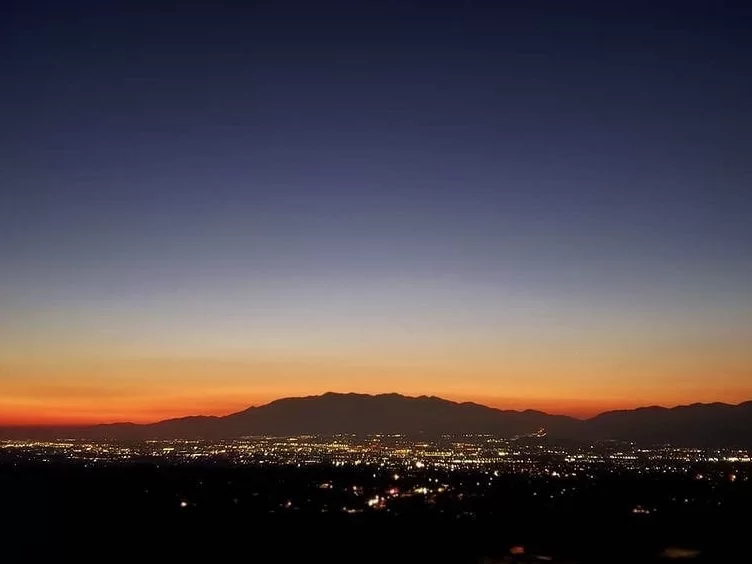 Panorama Point Matheran twilight panorama of distant city lights twinkling orange sunset over silhouetted mountains dark blue sky, perfect nightfall viewpoint, Maharashtra tour packages.