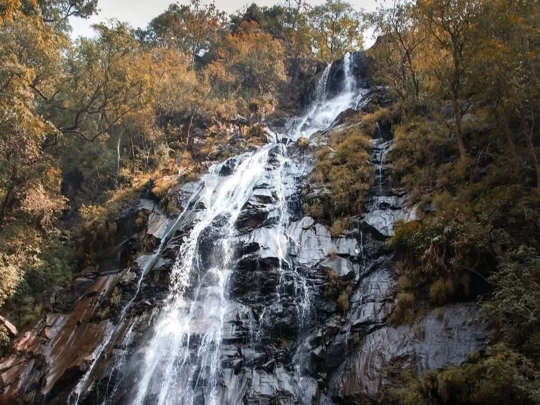 Bee Falls waterfall at Pachmarhi during autumn glow, featuring orange foliage forested cliffs cascade, perfect adventure experience Pachmarhi tour package.