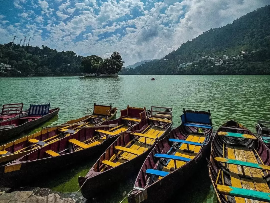 Colorful rowboats docked at Naukuchiatal Lake Nainital during sunny afternoon, featuring emerald waters and distant hills, perfect adventure experience Uttarakhand tour package.