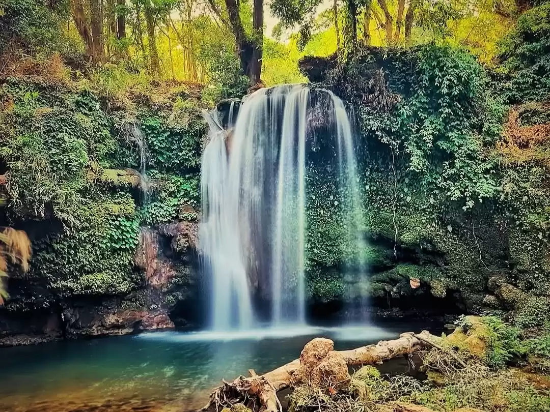 Jim Corbett Falls multi-tier waterfall lush jungle emerald pool rocks, misty cascade ivied cliffs trees golden sunlight turquoise water, perfect Uttarakhand tour packages.