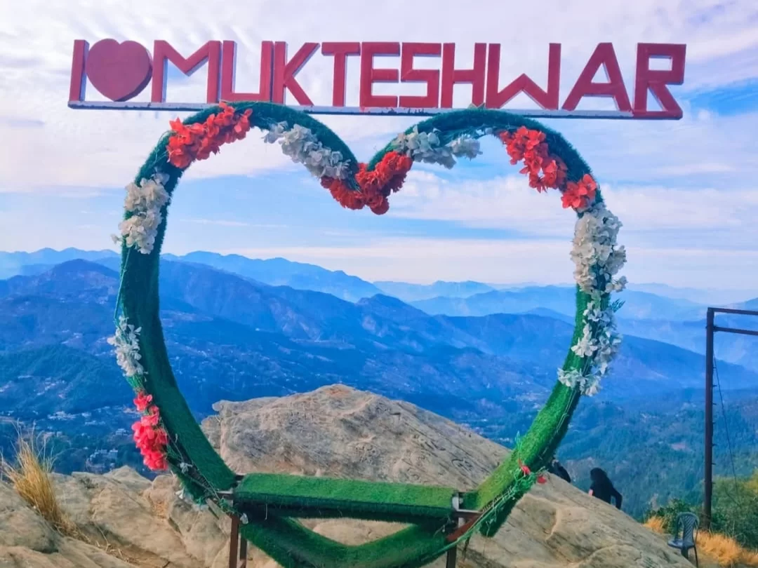 I love Mukteshwar floral arch sign during sunny weather, featuring red letters heart frame, Himalayan mountains, perfect spiritual adventure, Uttarakhand tour packages.