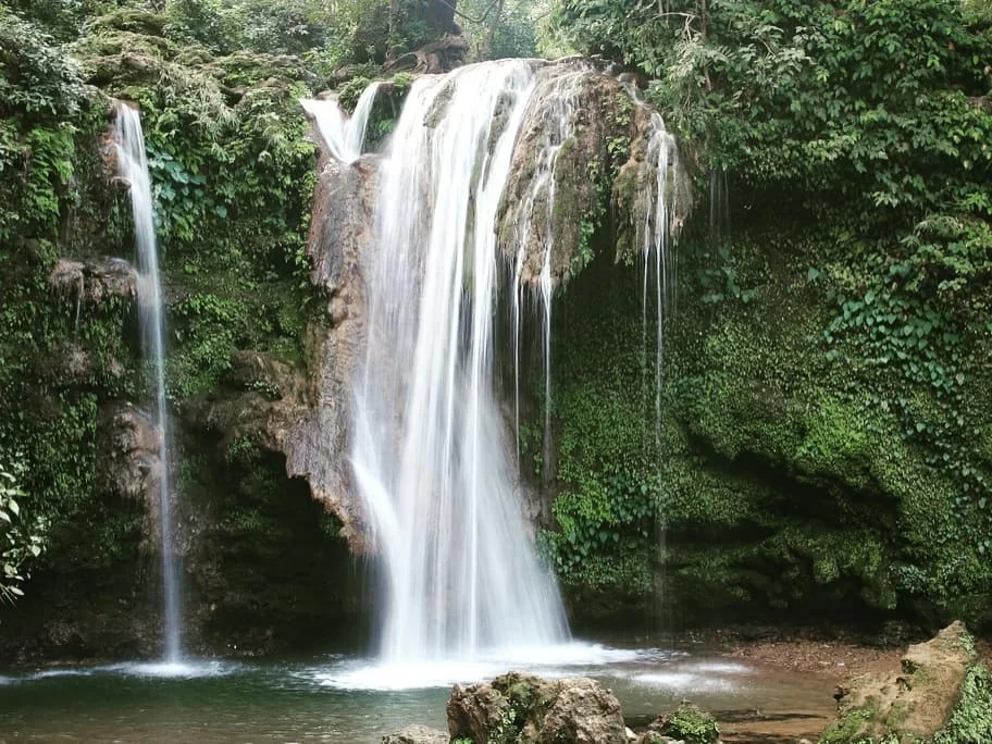 Rudradhari Waterfall Kausani lush green forested multi-tiered cascade into plunge pool rocky base tropical foliage, perfect trekking nature spot near Shiva cave temple, Uttarakhand tour packages.