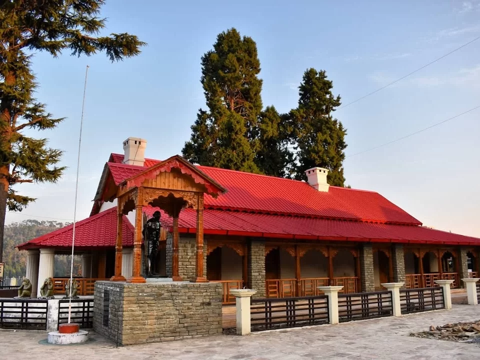 Anasakti Ashram Kausani traditional stone red tin roof cottage Gandhi statue wooden pavilion deodar pines blue sky mountains, perfect Gandhi stay heritage site, Uttarakhand tour packages.