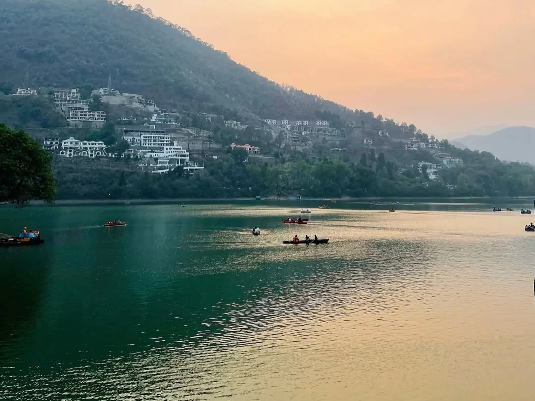 Bhimtal Lake sunset with boats on emerald waters, hillside hotels & hazy orange mountains, perfect romantic experience Uttarakhand tour packages.