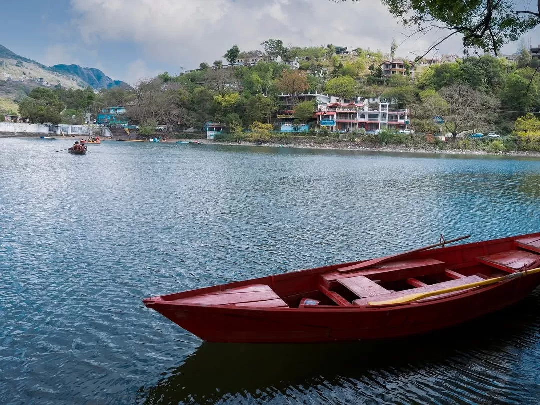 Red rowboat on Bhimtal Lake foreground with hill resorts backdrop & distant boats, perfect romantic experience Uttarakhand tour packages.
