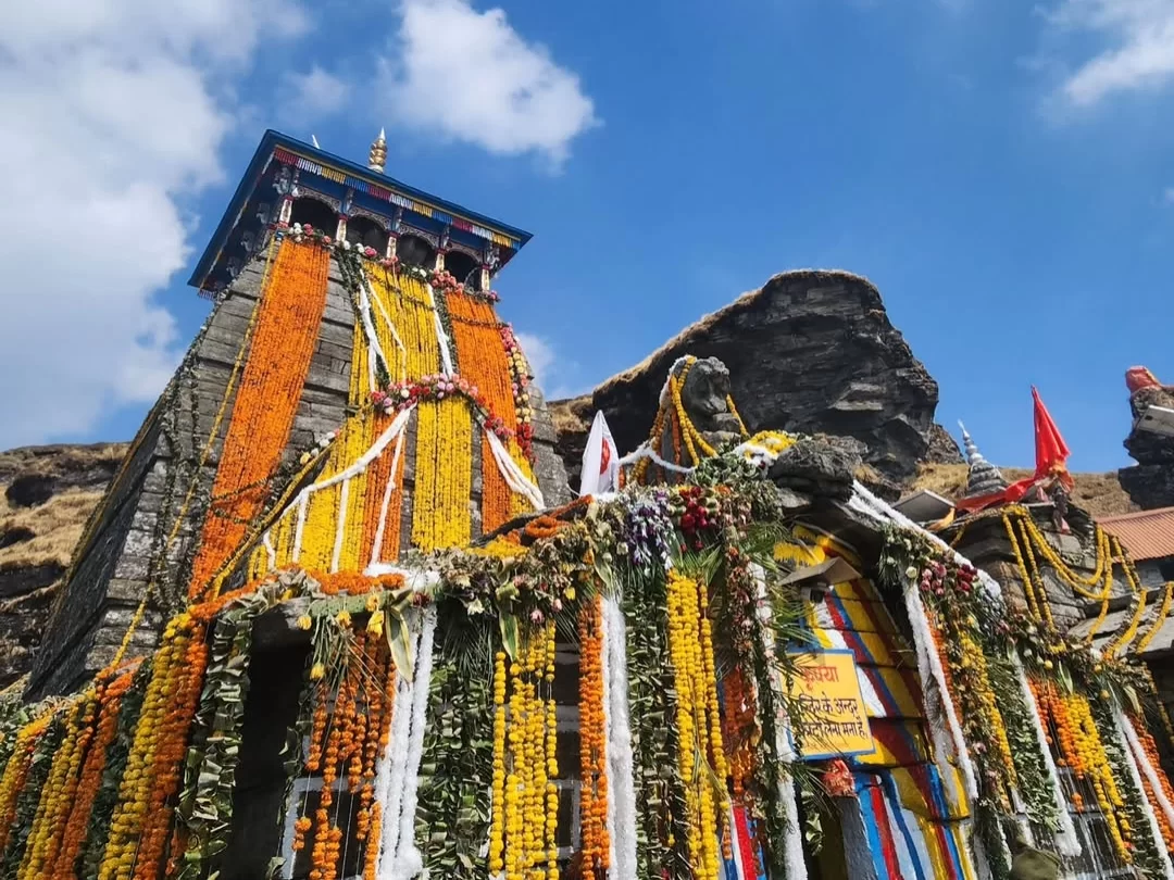 Tungnath Temple festooned with marigolds during clear sky, featuring garlands & rocky backdrop, perfect adventure experience Uttarakhand tour packages. 