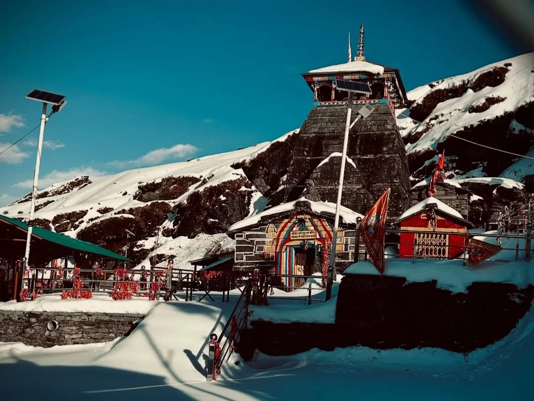 Tungnath Temple tower at snowy slopes during clear day, featuring prayer flags & colorful shrines, perfect adventure experience Uttarakhand tour packages.