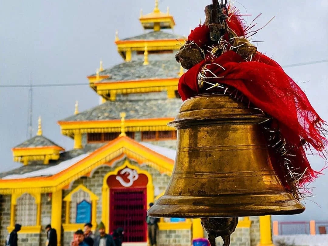 Temple bell at Maa Surkanda Devi Temple Dhanaulti during cloudy weather, featuring yellow pagoda, red scarf and devotees, perfect spiritual experience in Uttarakhand tour package.