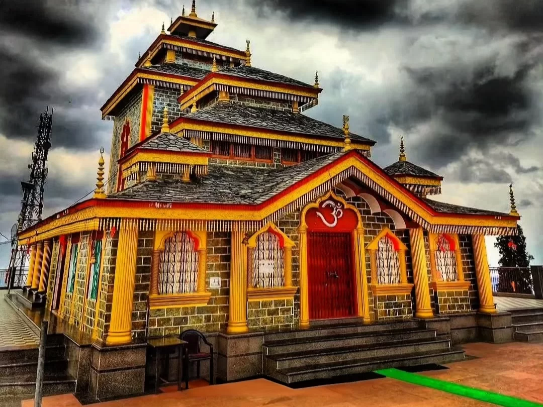 Maa Surkanda Devi Temple at Dhanaulti during dramatic clouds, featuring multi-tier pagoda, golden Om symbol and pillars, perfect spiritual experience in Uttarakhand tour package.
