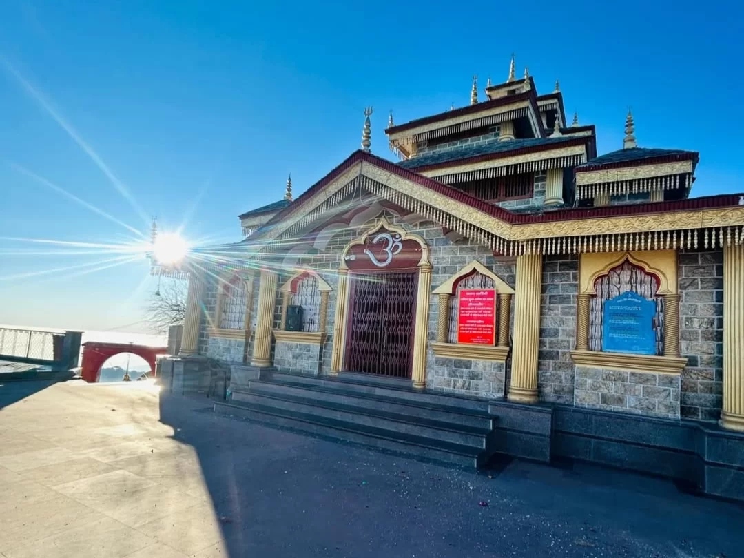 Maa Surkanda Devi Temple at Dhanaulti during sunny morning, featuring golden Om symbol, pagoda spires and bridge, perfect spiritual experience in Uttarakhand tour package.