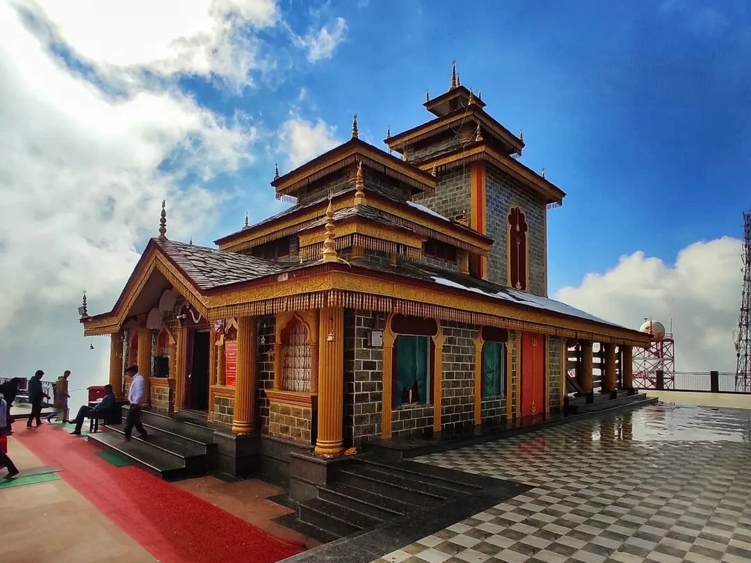 Ornate Maa Surkanda Devi Temple at Dhanaulti during partly cloudy day, featuring pagoda roofs, red carpet and devotees, perfect spiritual experience in Uttarakhand tour package.