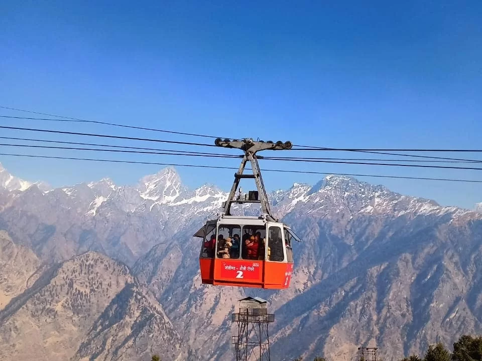 Cable car ride at Auli Ropeway during clear sunny day, featuring snow-capped Nanda Devi peaks mountains, perfect adventure experience Uttarakhand tour packages.