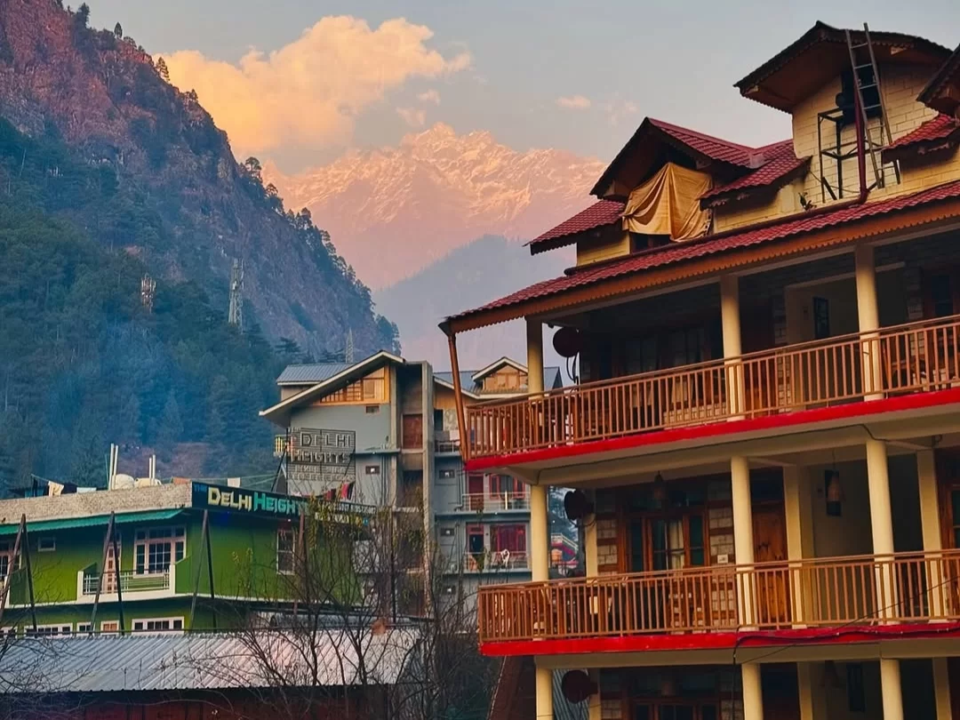 Bagori Village hotels during golden hour sunset Uttarkashi, featuring Dhaula Heights building red balcony houses against pink snowy mountains, perfect Uttarakhand tour packages.