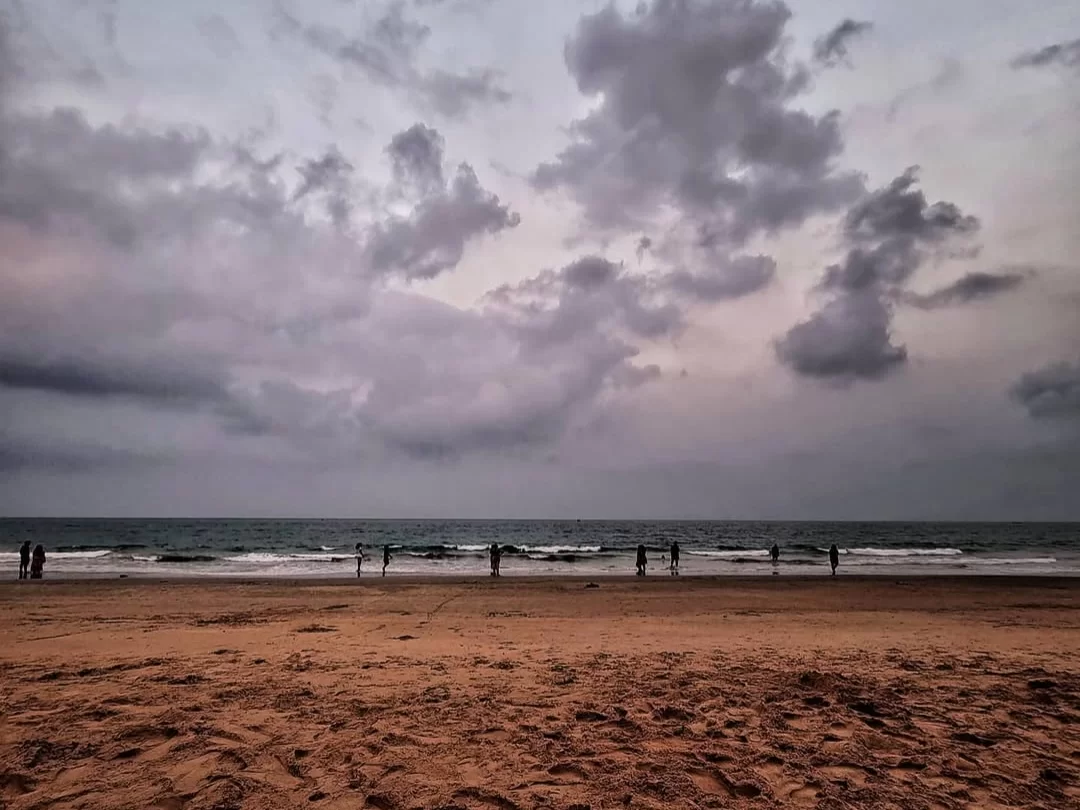 Majorda Beach Goa evening silhouettes distant walkers orange sands, dramatic cloudy skies endless ocean waves, perfect South Goa serene beach solitude package.