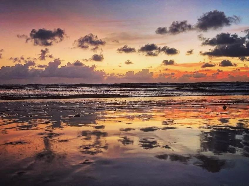 Majorda Beach Goa vibrant sunset reflection wet sands orange purple skies, fluffy clouds ocean waves mirror glow, perfect South Goa romantic beach sunset package. 