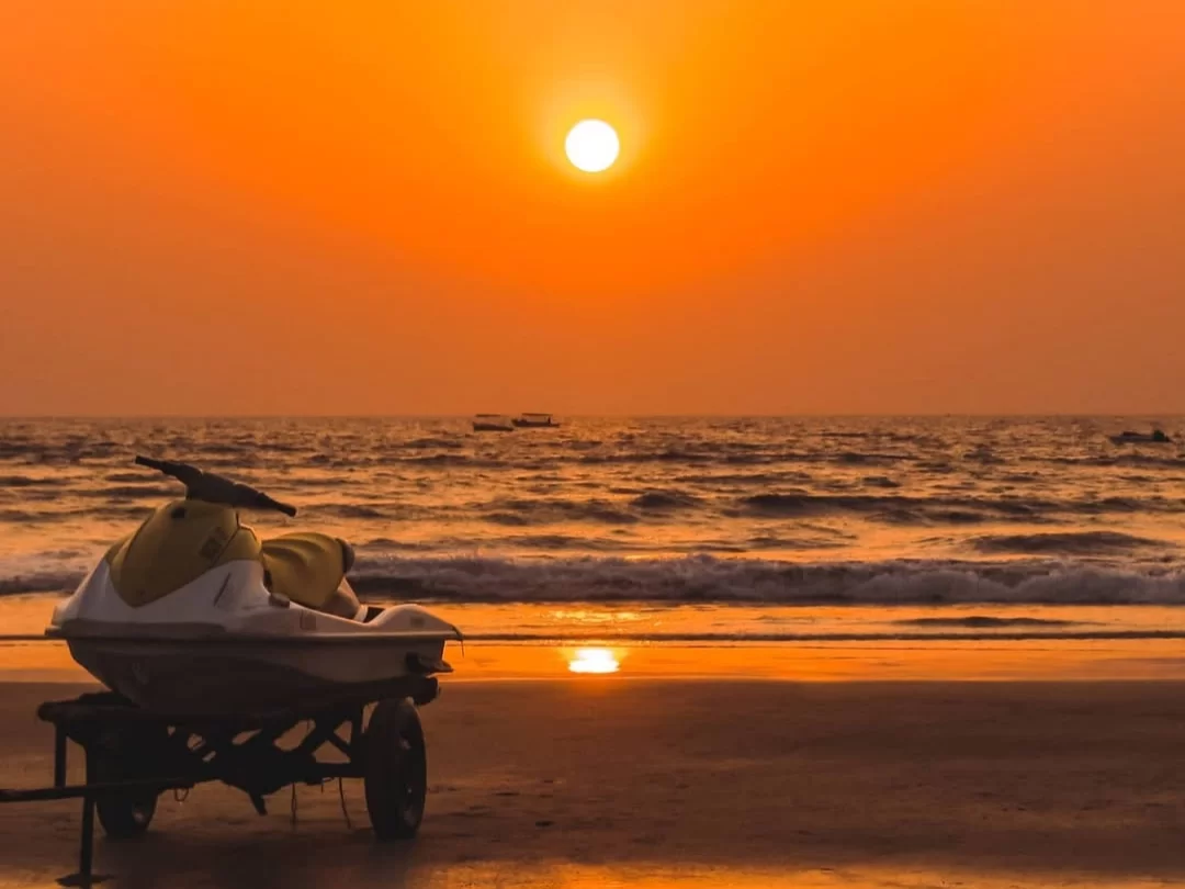 Yellow jet ski parked on Benaulim Beach Goa during vibrant orange sunset, featuring distant boats ocean waves golden reflections, perfect South Goa tour package. 