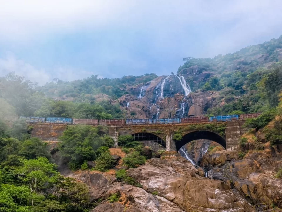 Dudhsagar Waterfall Goa train crossing iron bridge misty cascades, blue train lush green hills white streams Western Ghats, perfect Goa Karnataka border waterfall package.
