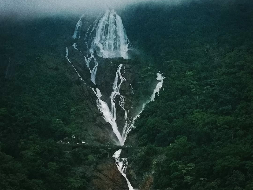 Dudhsagar Waterfall Goa misty aerial massive white cascades lush green forests, railway bridge foggy Western Ghats hills, perfect Goa monsoon milk waterfall package.