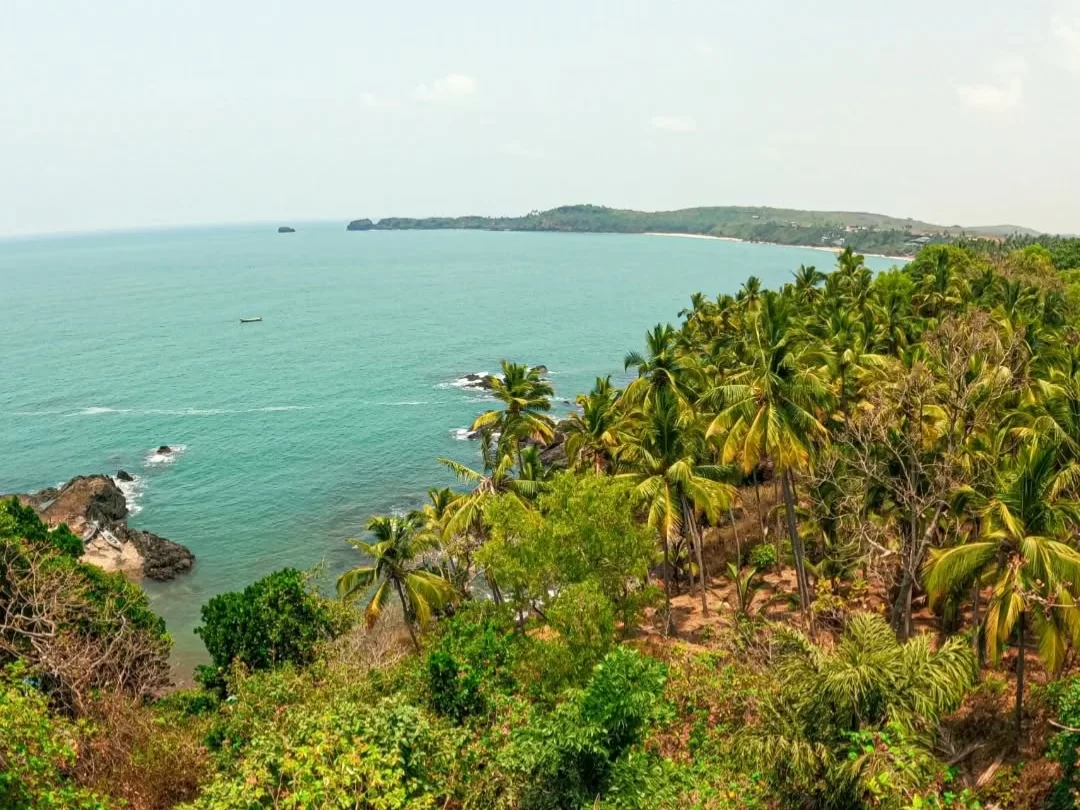 Panoramic ocean vista Cabo de Rama Fort Goa viewpoint, featuring turquoise Arabian Sea swaying palm trees rocky shoreline distant headland, perfect South Goa beach fort tour package.