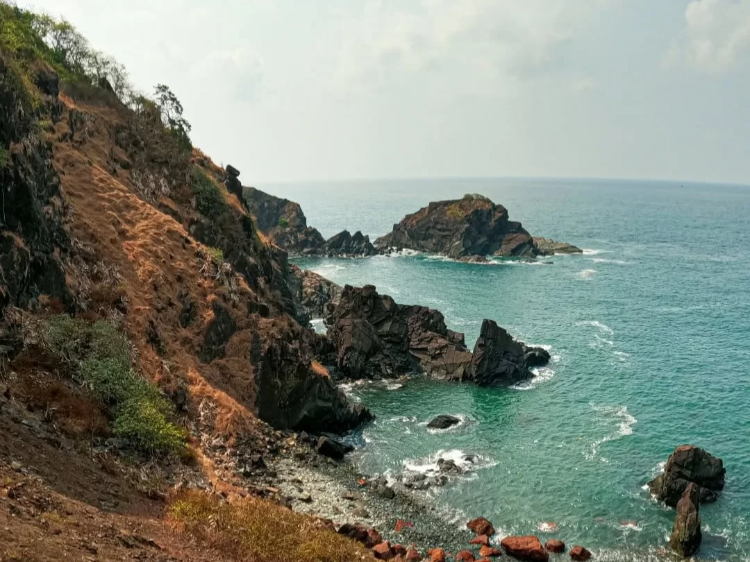 Rugged cliff edge Cabo de Rama Fort Goa overcast day, featuring emerald green sea dramatic rock outcrops sparse vegetation red soil path, perfect South Goa scenic fort tour package.