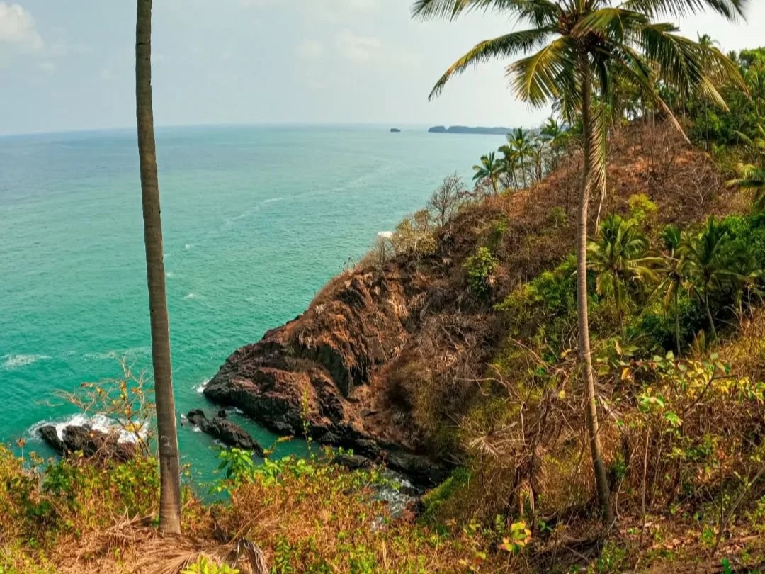 Tall palm trees framing Cabo de Rama Fort Goa sea view, featuring azure Arabian Sea rocky headland distant islands green hills, perfect South Goa panoramic fort tour package.