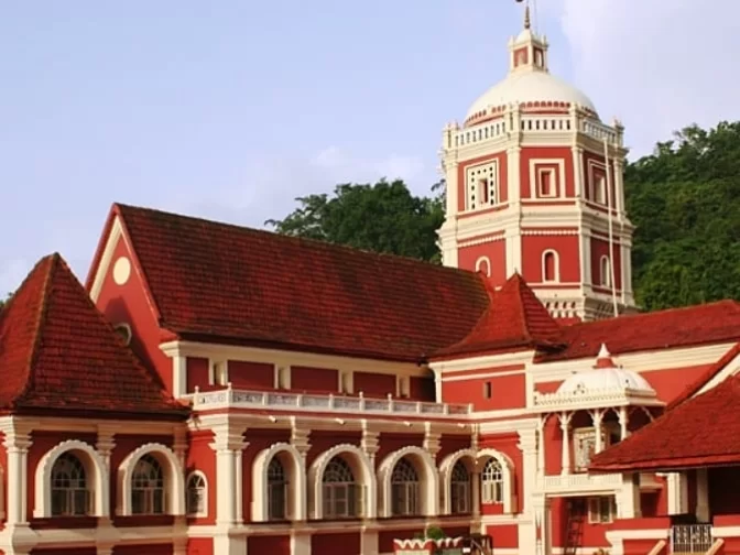 Iconic red tower at Shri Shantadurga Temple Kavlem Goa during clear day, featuring ornate arches tiled roofs and green hills, perfect spiritual Goa tour package.