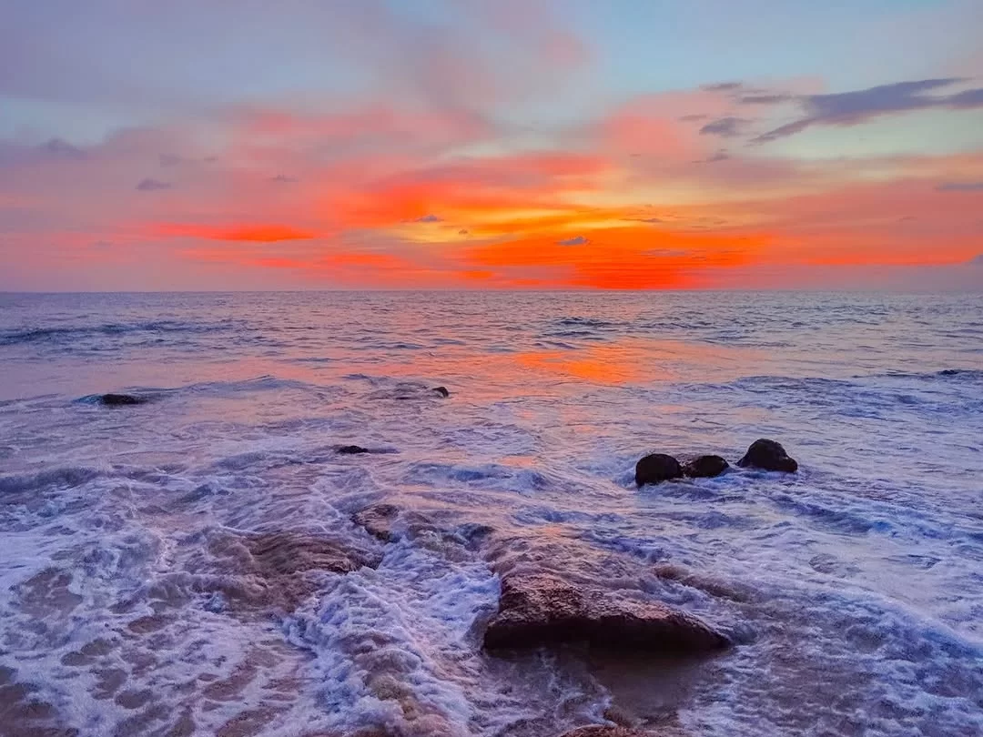 Vibrant sunset waves and rocks at Caranzalem Beach Goa during twilight, featuring pink orange sky foam sea, perfect romantic experience Goa beach tour package. 