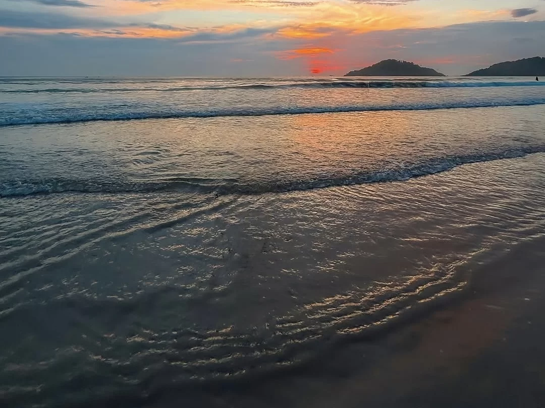 Dramatic sunset over waves and rocks at Caranzalem Beach Goa during twilight, featuring red sun clouds silhouettes, perfect romantic experience Goa beach tour package.