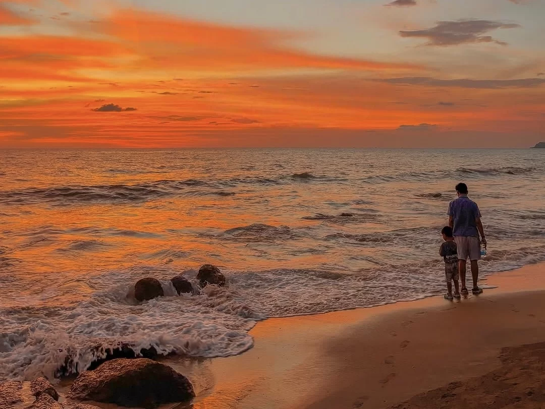 Father and son walking at Caranzalem Beach Goa during orange sunset, featuring waves rocks glowing sky, perfect family experience Goa beach tour package.