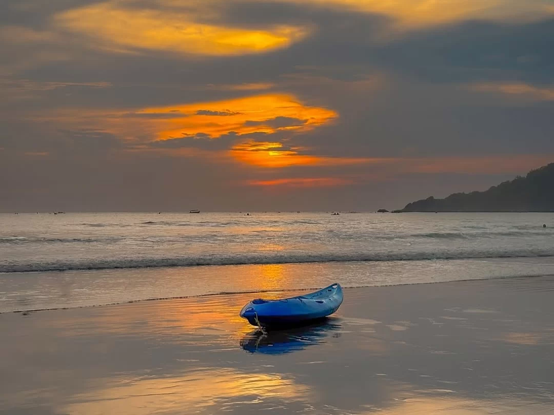Blue kayak on shore at Caranzalem Beach Goa during dramatic sunset, featuring orange clouds sun reflection waves, perfect adventure experience Goa beach tour package. 