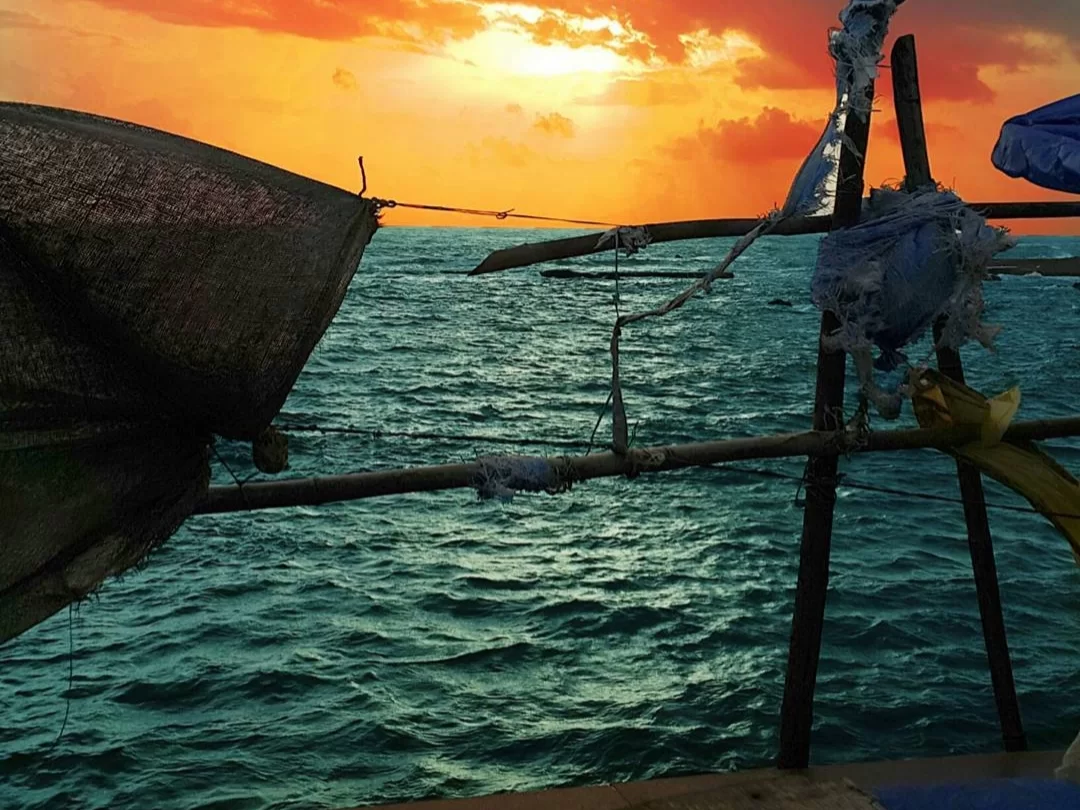 Fishing net sail at Dona Paula Beach Goa during orange sunset, featuring wooden poles blue sea horizon, perfect cultural experience Goa beach tour package. 