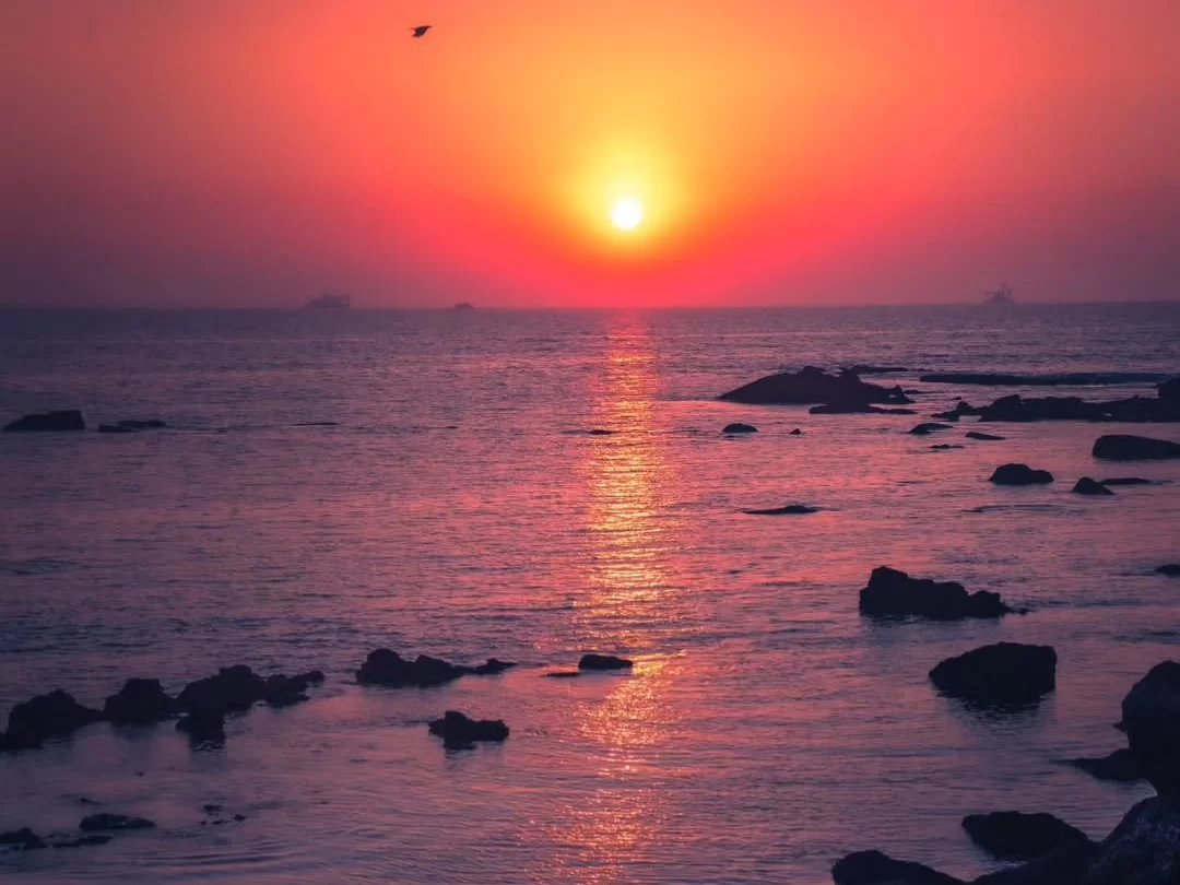 Fiery red sunset over rocky sea at Dona Paula Beach Goa during twilight, featuring bird reflection rocks waves, perfect romantic experience Goa beach tour package.