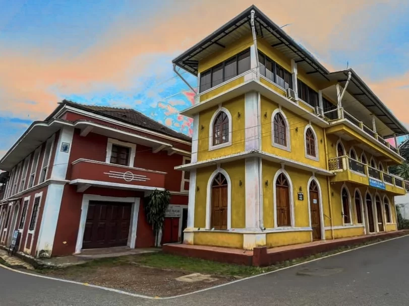Classic yellow Portuguese colonial house in Fontainhas Latin Quarter Panaji Goa, featuring white pillars balconies potted plants rainy street, perfect heritage experience Goa heritage walking tour package.