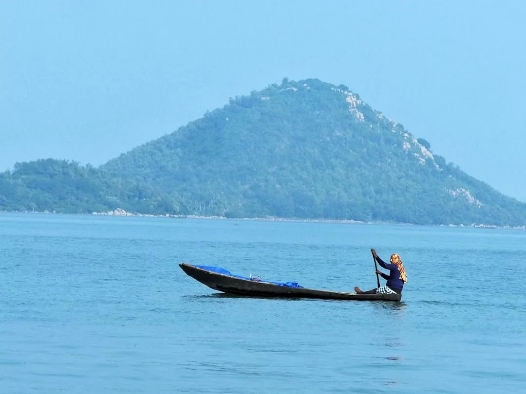 Chilika Lake Odisha woman paddling traditional boat distant lush hill mountain backdrop serene waters, perfect Puri birdwatching dolphin safari tour package.