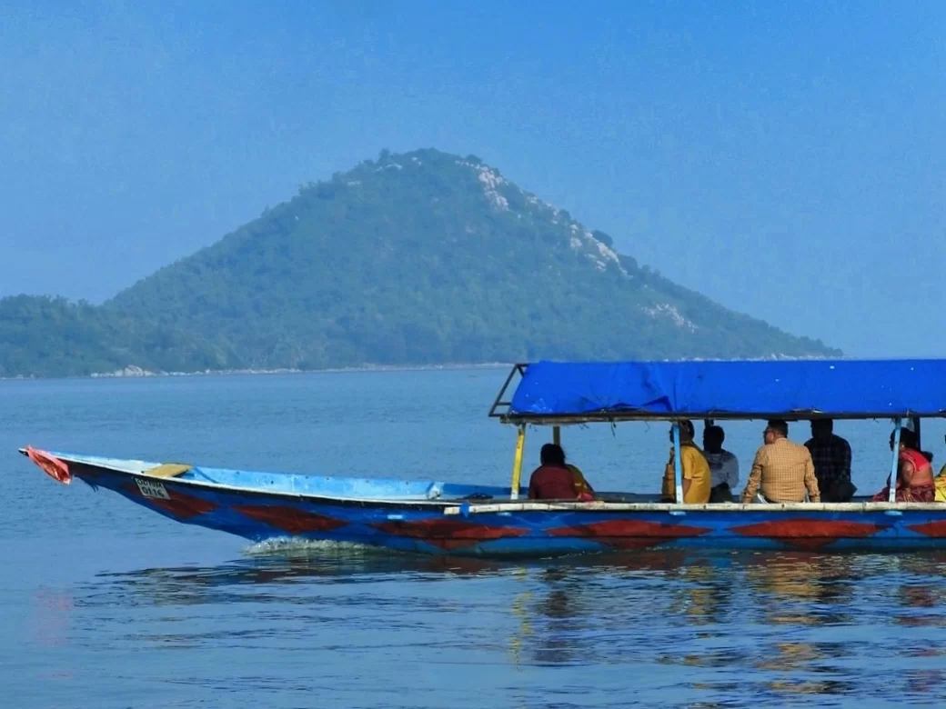 Chilika Lake Odisha colorful blue tourist boat passengers distant green hill mountain backdrop serene waters, perfect Puri birdwatching dolphin safari tour package. 