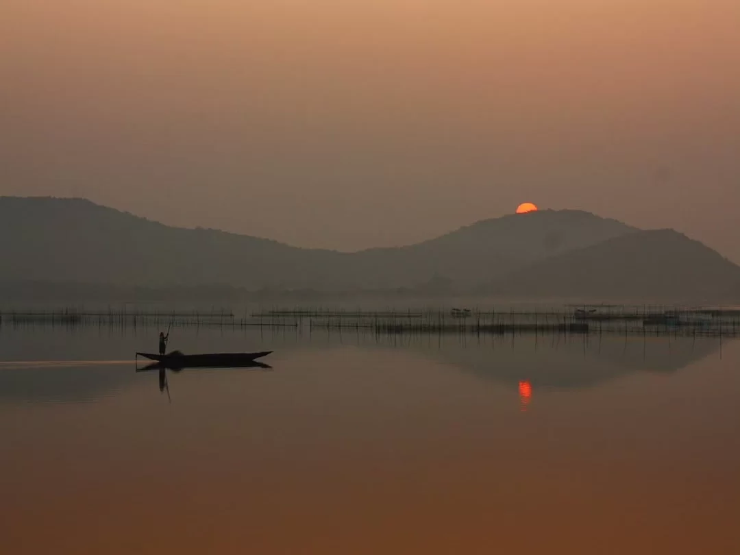Chilika Lake Odisha fisherman boat sunset silhouette distant hills mountains bamboo fishing nets water reflection serene lagoon, perfect Puri birdwatching dolphin safari tour package.