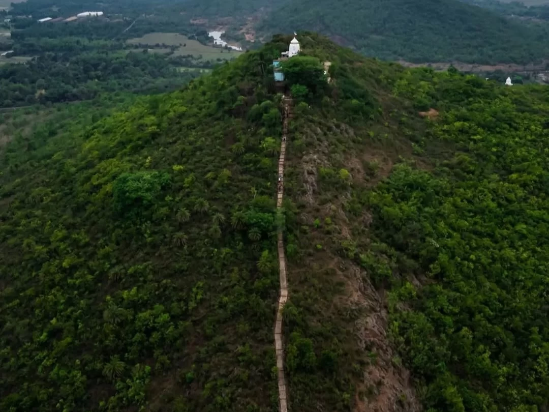 Aerial view of Biswanath Temple at Biswanath Mundia Hill Delang Puri Odisha during cloudy weather, featuring white shikhara, stone trail, river valley, forested slopes, perfect heritage experience Odisha tour package. 