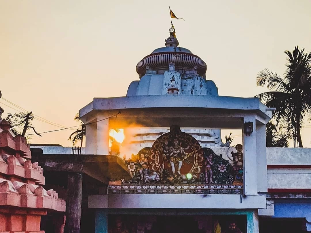 Markandeswar Temple Puri Odisha white shikhara with golden flag at sunset, Krishna sculpture centerpiece, palm trees silhouetted against orange sky glow, perfect Jagannath heritage India tour package