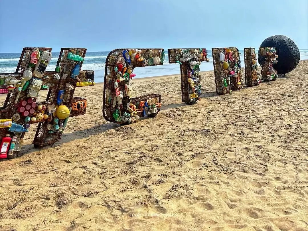 Puri Beach during clear daytime, featuring recycled plastic letters, beach sand, ocean waves, perfect eco-tourism experience with Odisha Puri tour package.