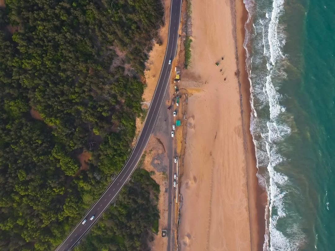 Puri Konark Marine Drive Odisha drone aerial highway golden beach crashing waves palms, construction vehicles turquoise ocean lush greenery, perfect coastal scenic drive package.