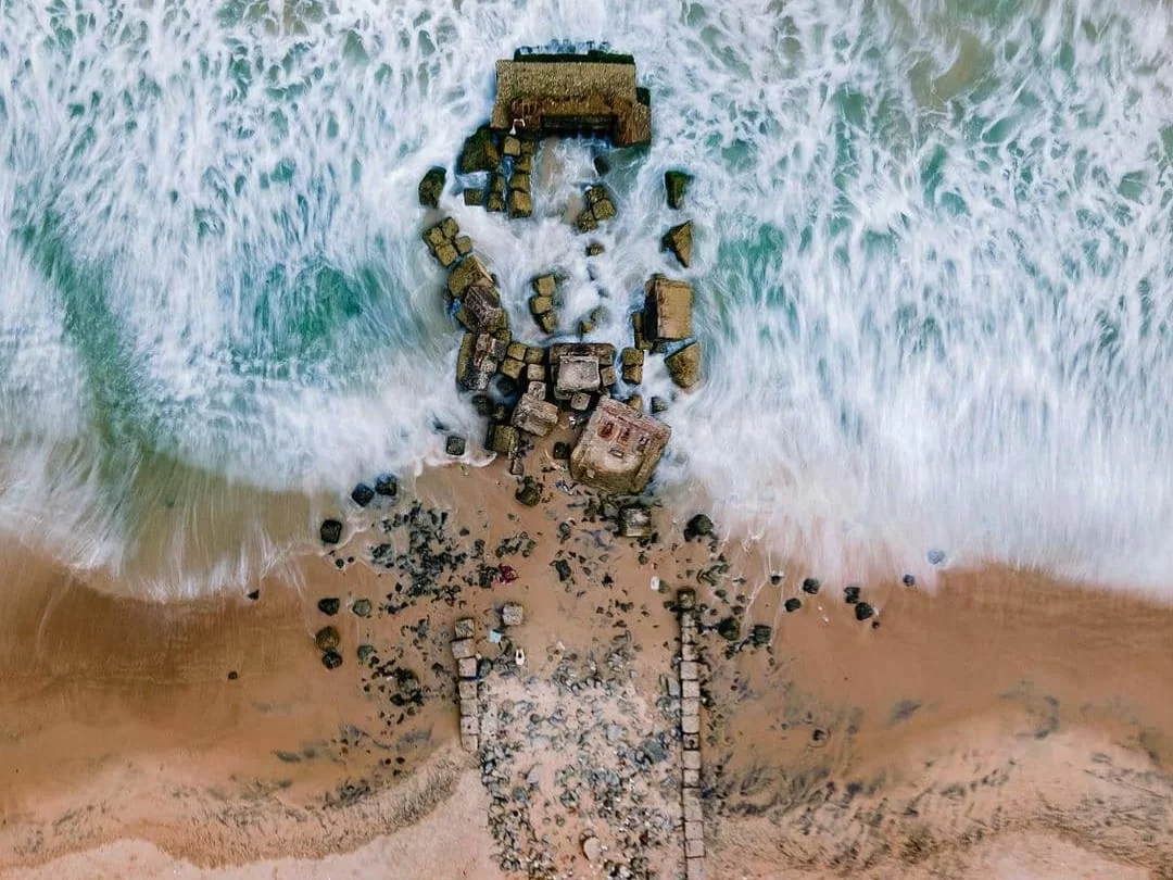 Chandrabhaga Beach Odisha aerial view ruined breakwater crashing turquoise waves sandy shore rocky outcrops blue ocean golden sand, perfect beach experience for Konark Chandrabhaga tour package