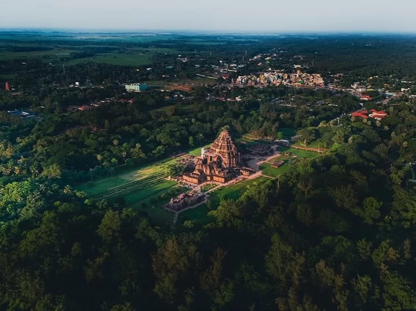 Aerial view of Konark Sun Temple Odisha during golden hour, featuring chariot wheels, stone horses, lush forests, ocean horizon, perfect heritage experience Odisha tour package.