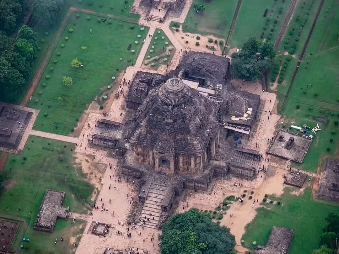 Aerial view of Konark Sun Temple Odisha during clear day, featuring main deul tower, jagamohana, stone wheels, gardens, crowds, forests, perfect heritage experience Odisha tour package.