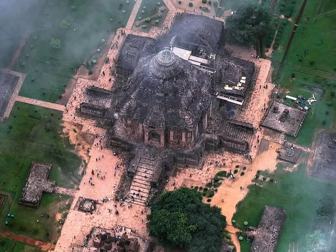 Aerial view of Konark Sun Temple Odisha during misty weather, featuring main deul tower, jagamohana, stone wheels, gardens, crowds, forests, perfect heritage experience Odisha tour package. 