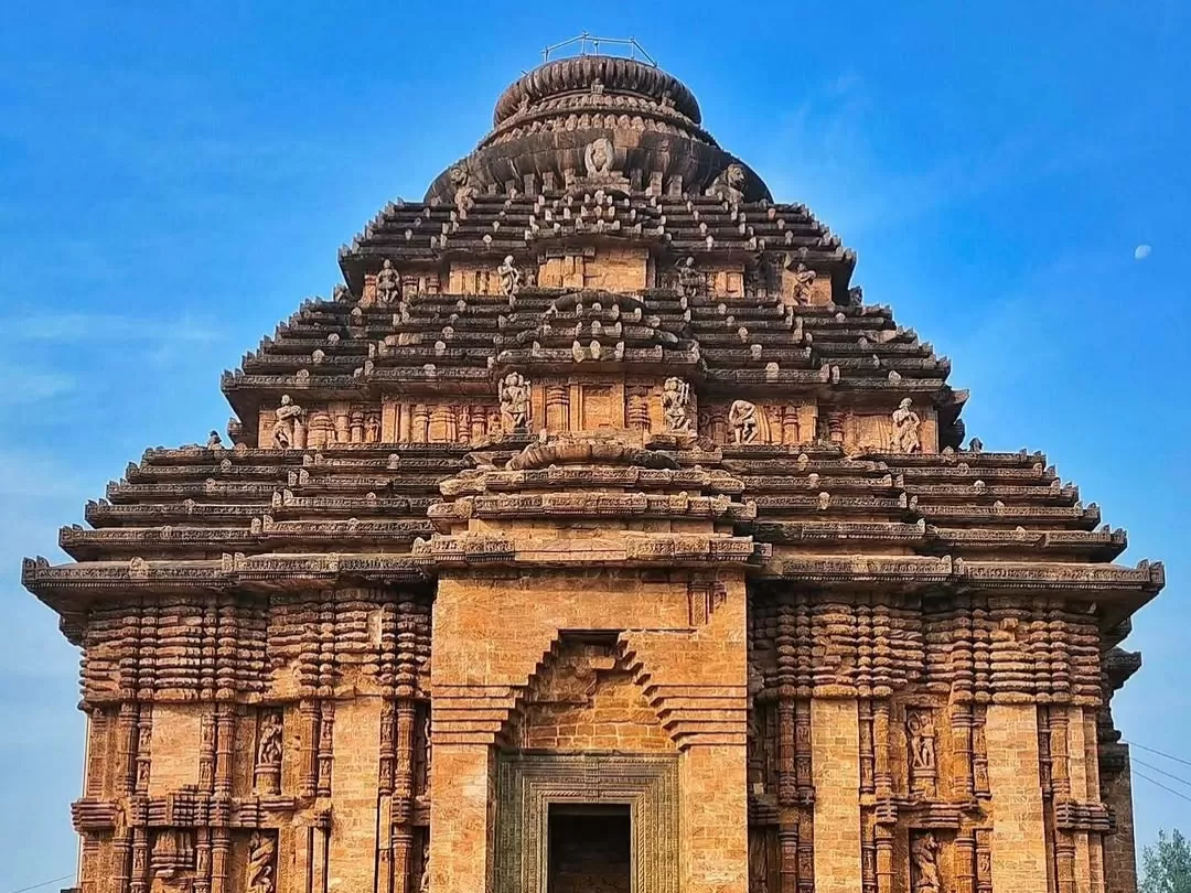 Jagamohana tower at Konark Sun Temple Odisha during clear skies, featuring multi-tiered shikhara, carved deities, entrance arch, greenery, perfect heritage experience Odisha tour package. 