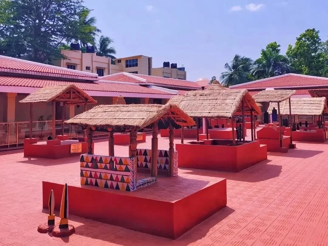 Odisha State Tribal Museum Bhubaneswar outdoor red thatched tribal huts complex geometric patterns palms blue sky, perfect Odisha tribal heritage culture tour package. 